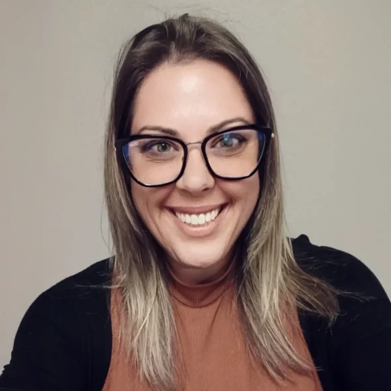Woman with glasses smiling at the camera, wearing a brown top and black cardigan.