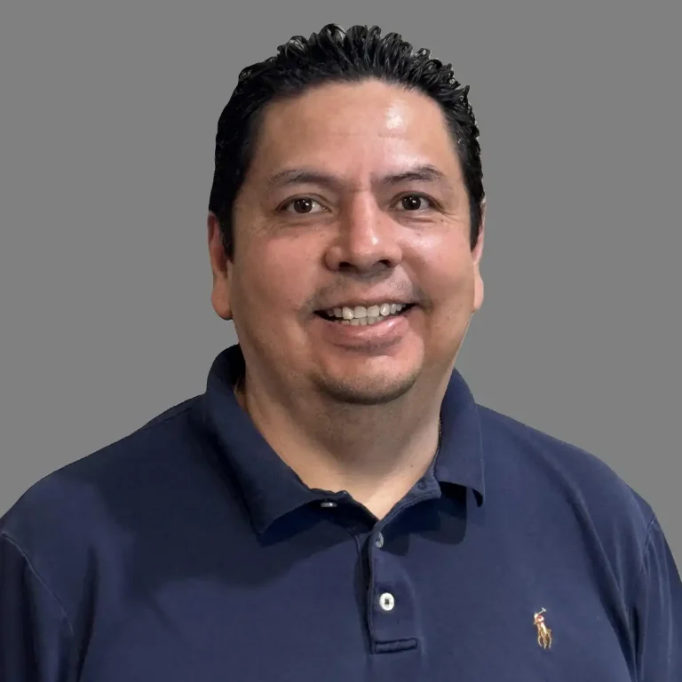 A man in a navy polo shirt smiling against a gray background.
