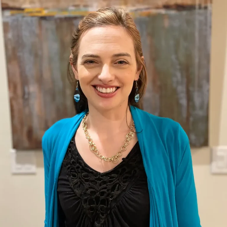 Person in a blue cardigan smiling in front of a textured wall art piece.