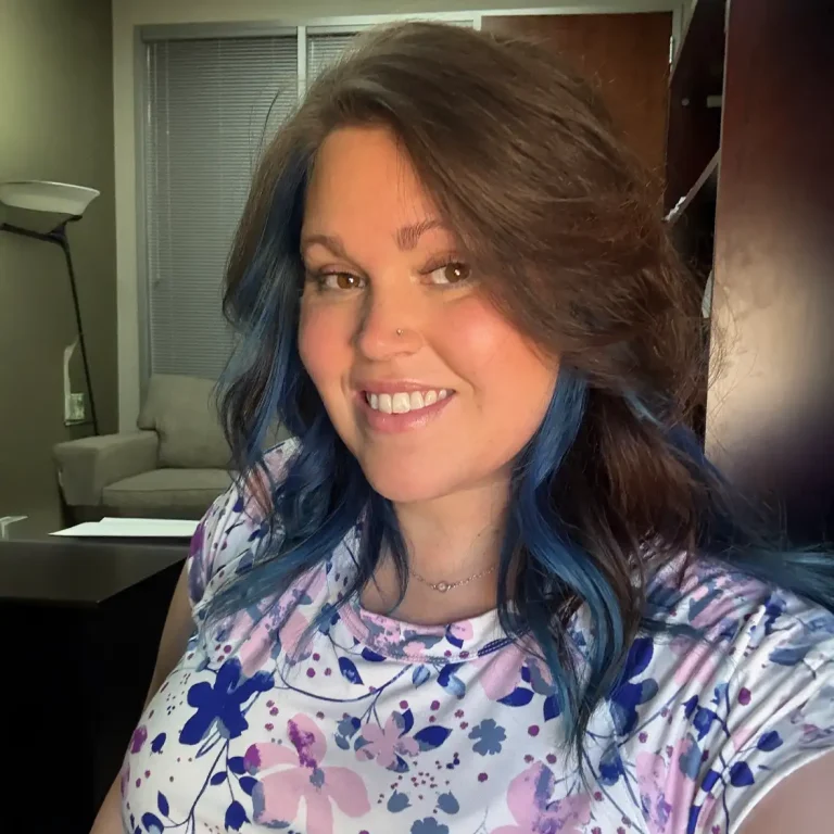 Woman with brown hair and blue highlights smiling in an office.